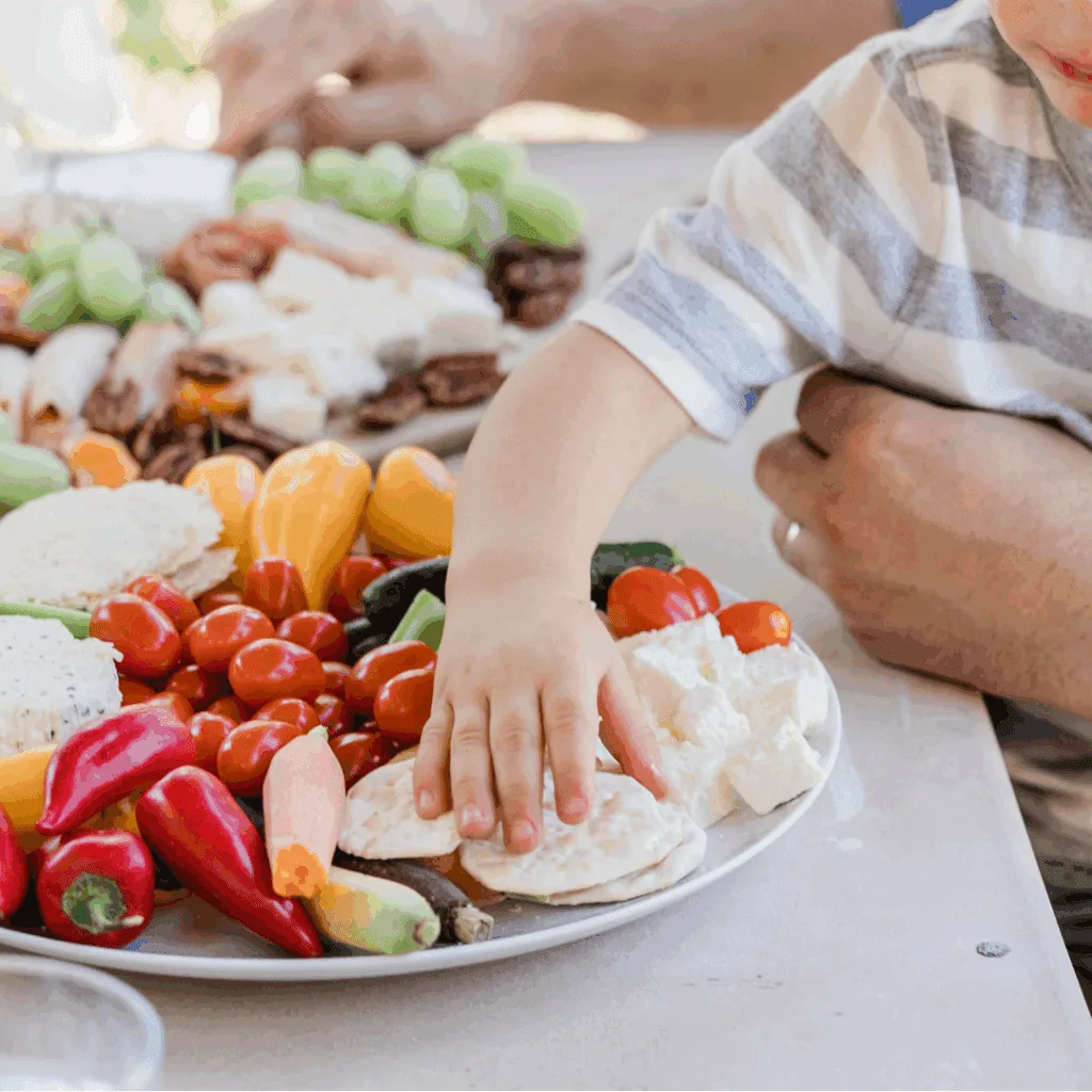 Child reaching for a platter of fresh fruit and vegetables