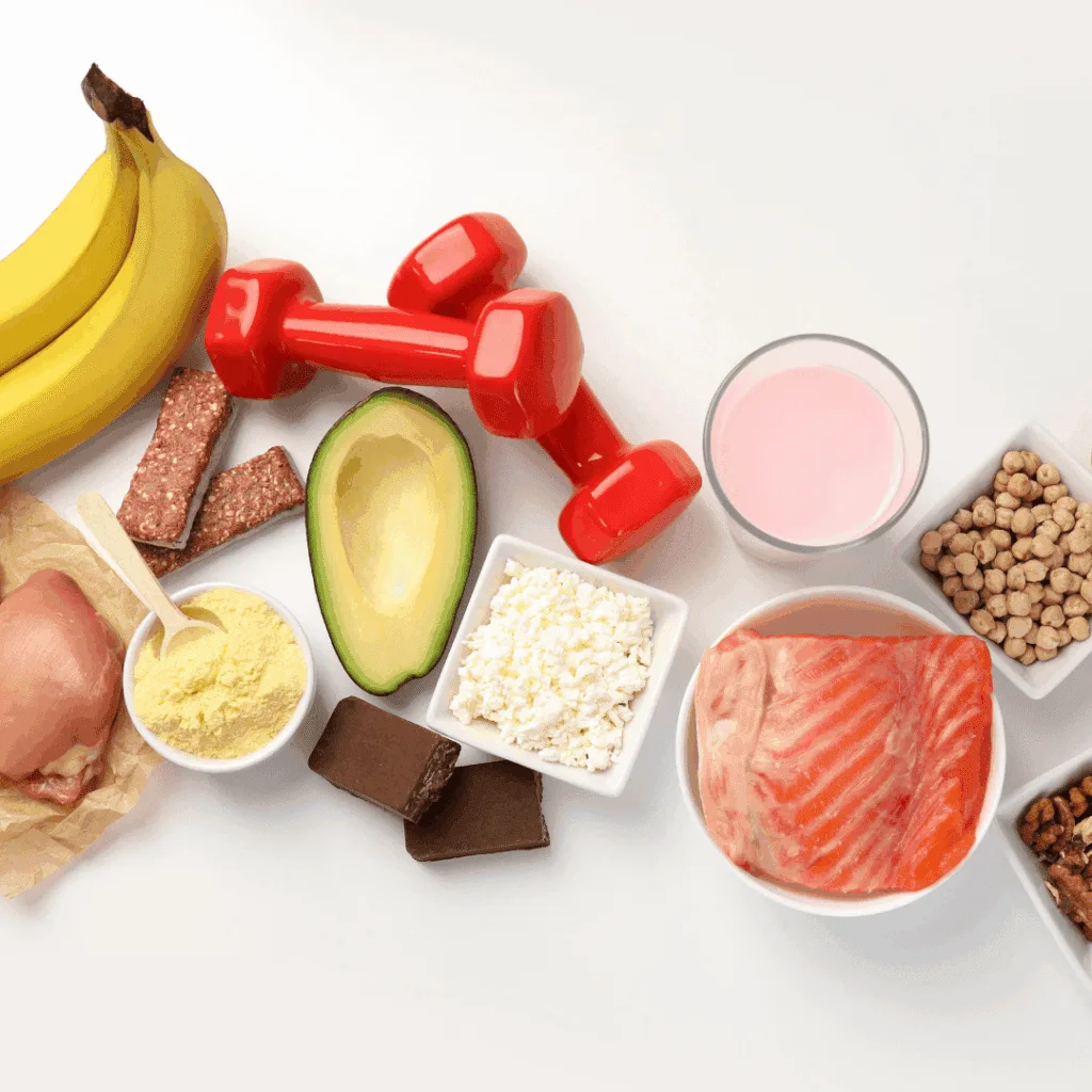Bananas, salmon, avocado, eggs and a smoothie beside a pair of dumbbells