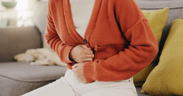 Person in an orange jumper holding their stomach in discomfort